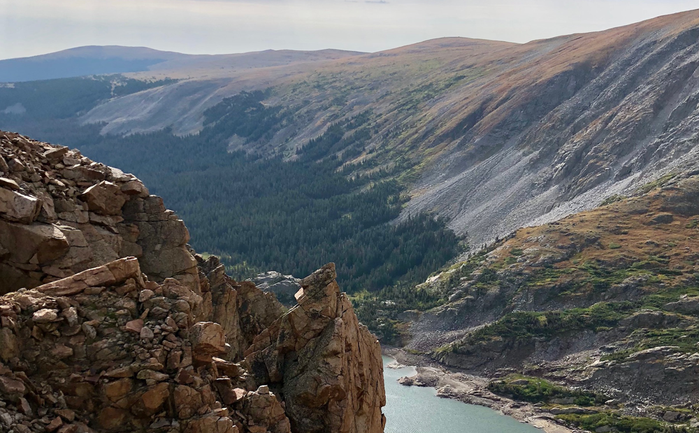 Scenic view of a rocky mountain ridge overlooking a lush forested valley with a winding river, under a clear sky.